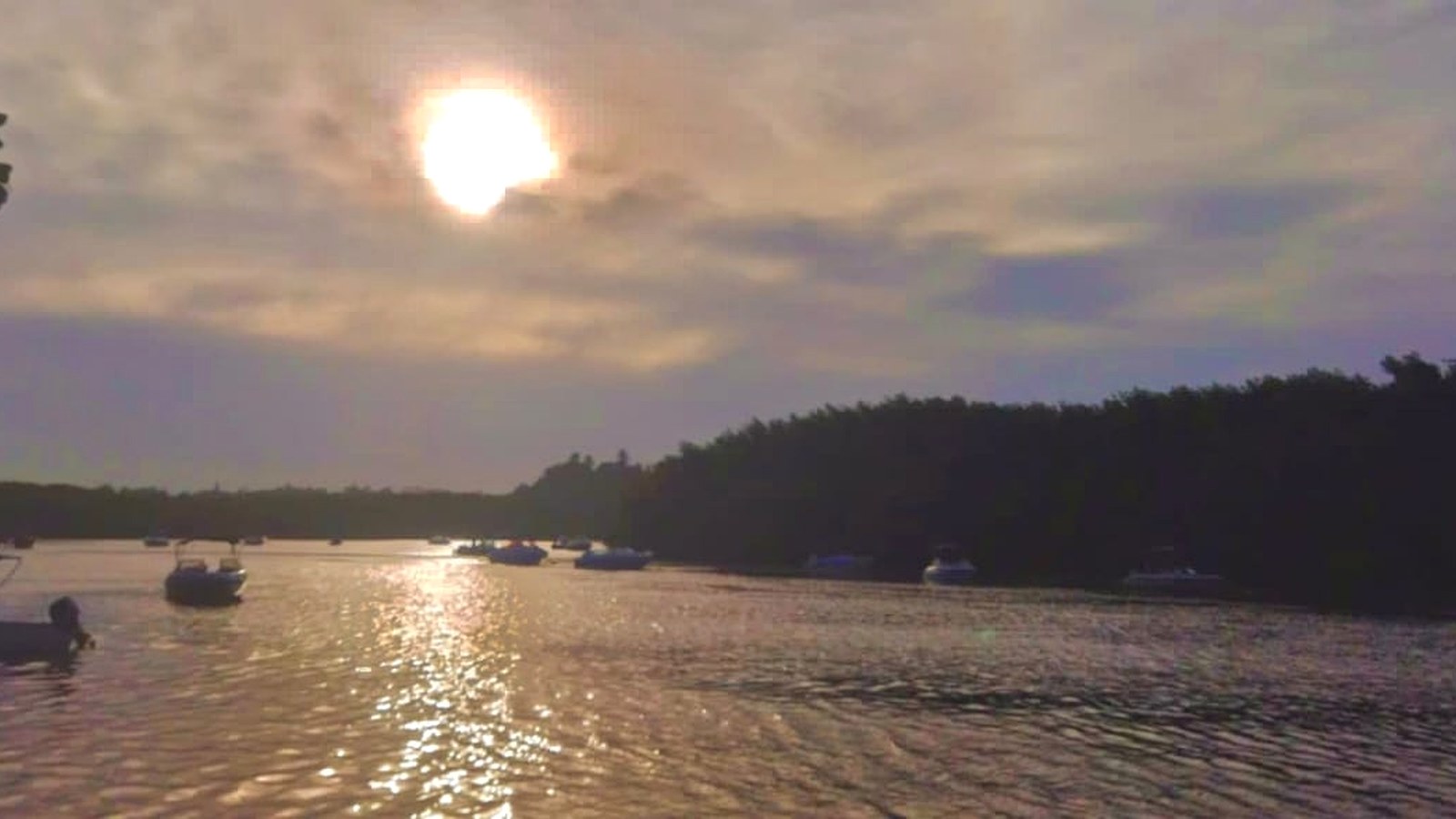 Fim de tarde no rio Caraíva, com barcos sobre a água, vegetação nas margens e a luz do sol refletida no rio.